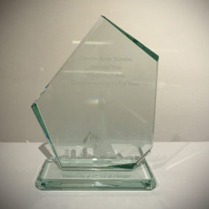 Glass engraved award in the shape of a distorted pentagon that says Francine Renee Manilow Inducted Into The Chicago Area Entrepreneurship Hall of Fame. The base of the award is engraved with the words University of Illinois Chicago