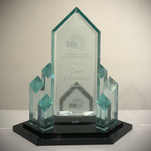 A glass award in the shape of a tall building with a pointed top, with several small glass towers at the base. The glass is engraved with Corporate Housing Providers Association Tower of Excellence Award. Francine Manilow Manilow Suites. Provider Member of the Year - Company 2008