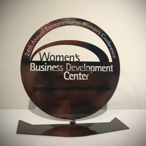 A circle shaped brown award that is engraved with the words 24th Annual Entrepreneurial Women's Conference, Women's Business Development Center. 2010 Entrepreneurial Woman of the Year